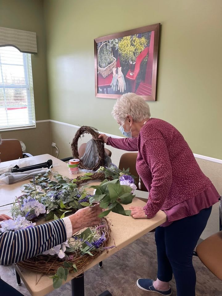 A group of seniors engaging in a wreath-making workshop, arranging flowers and greenery indoors.