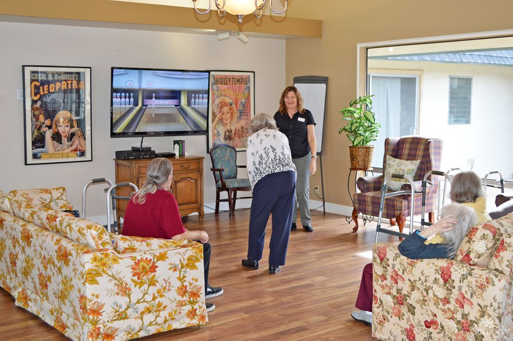 A group of elderly people engaging in an activity at a community center, with a television and seating area visible.
