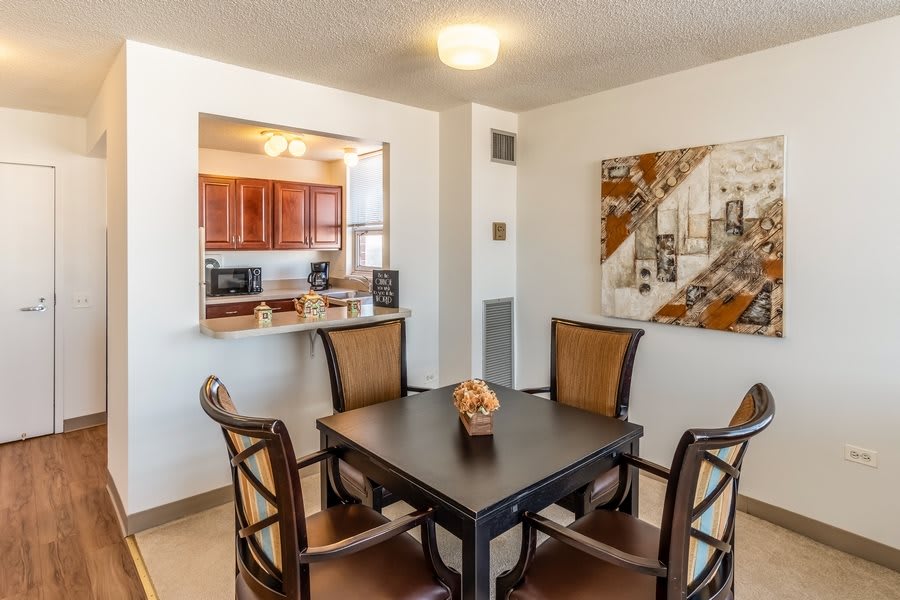 A modern dining area with a table and four chairs, featuring a view into the kitchen.