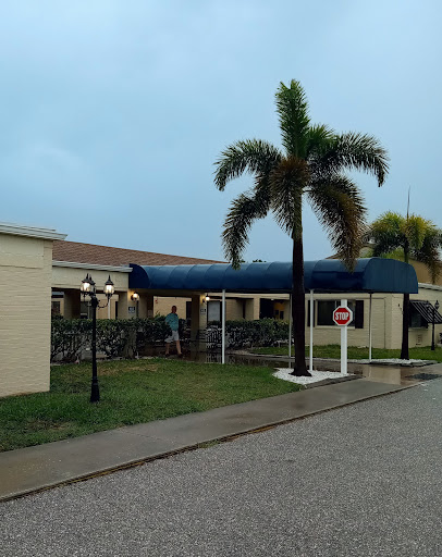 A view of a building entrance with palm trees under a cloudy sky.