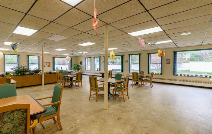 A spacious dining area with tables and chairs, featuring large windows and overhead lighting.