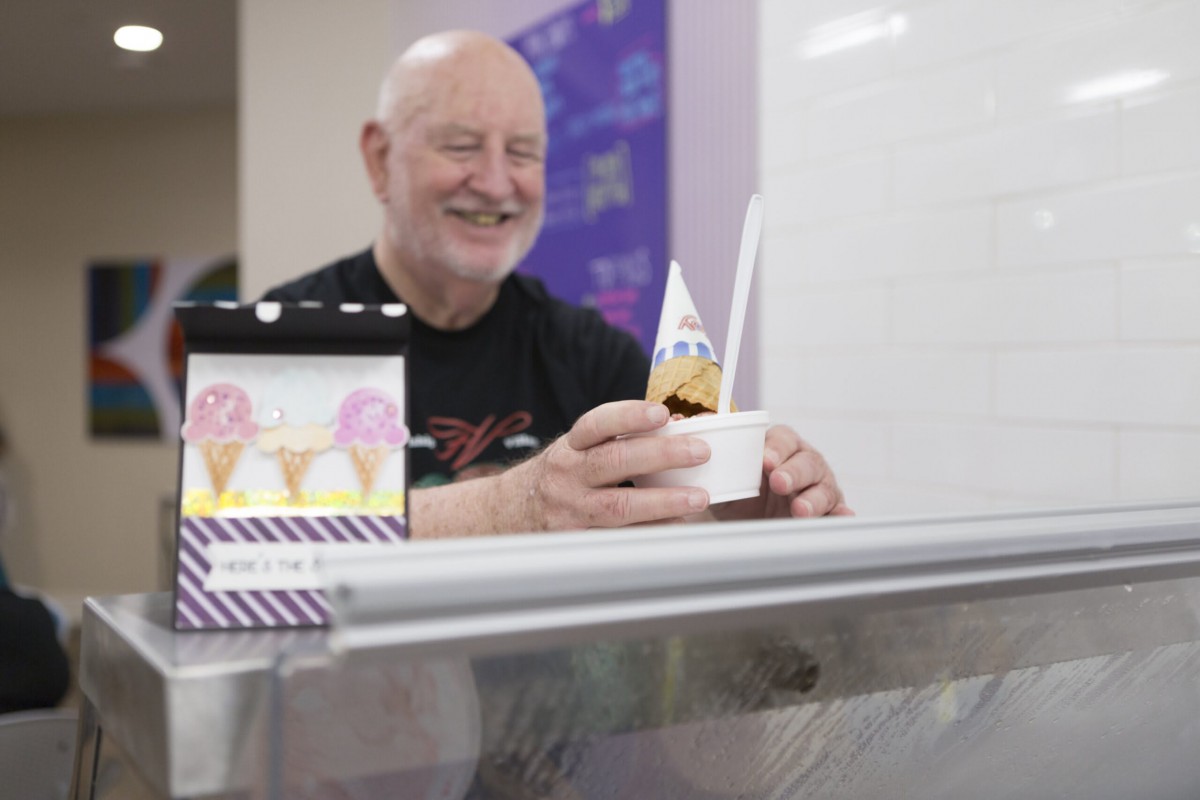 A man happily serves ice cream at a dessert shop.
