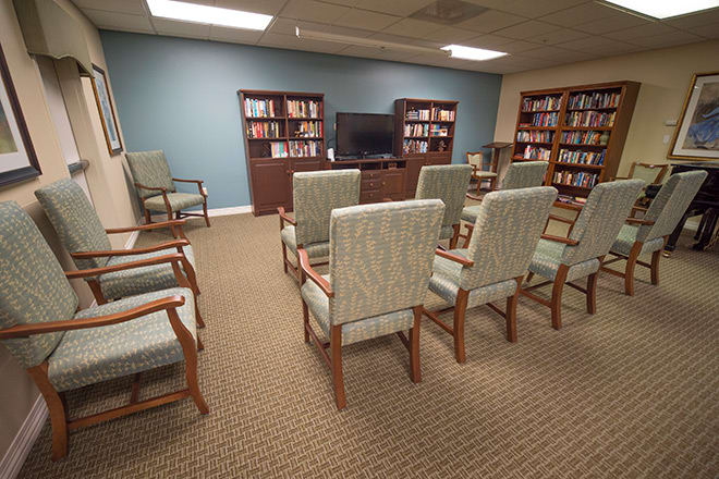 A cozy library room with arranged chairs facing a television and bookshelves filled with books.