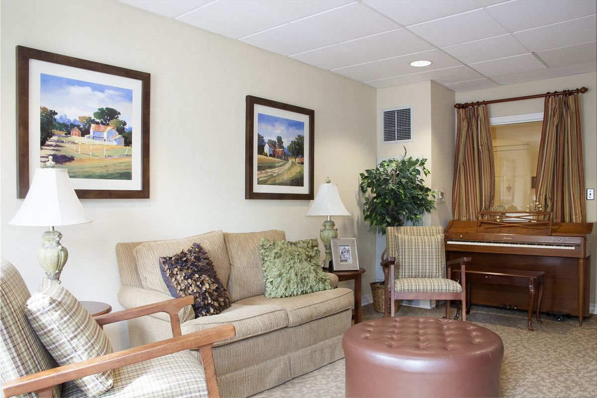 A cozy living room featuring a sofa, artwork, and a piano.