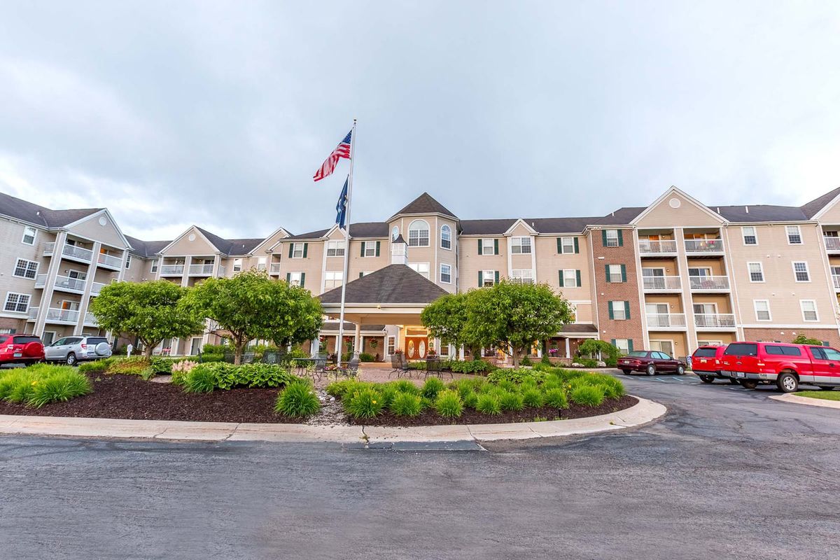 A hotel building with flags flying in front, surrounded by well-maintained landscaping and trees on a cloudy day.