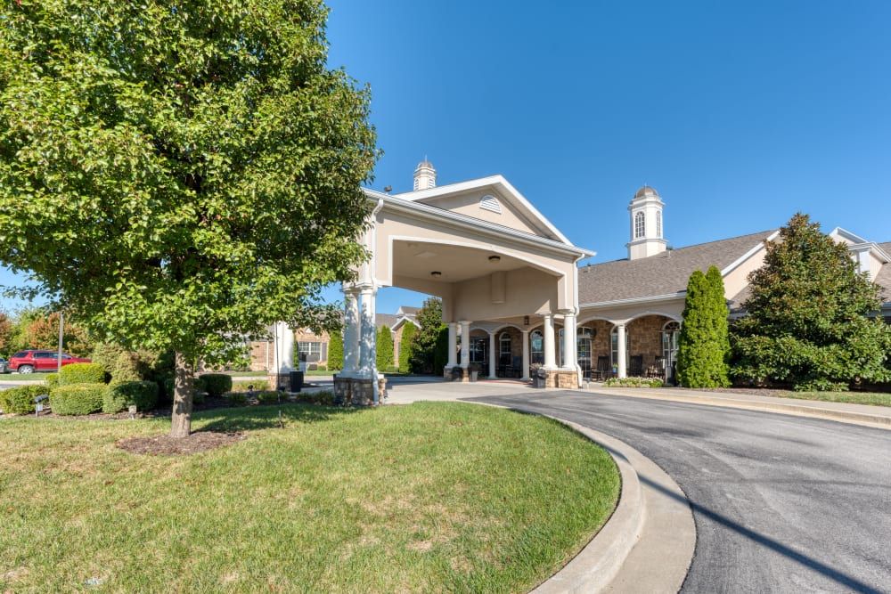 A large building entrance with a covered driveway and surrounding greenery on a sunny day.