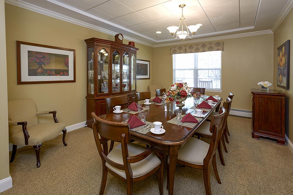 A formal dining room featuring a long table set for a meal, surrounded by chairs and illuminated by a ceiling light.