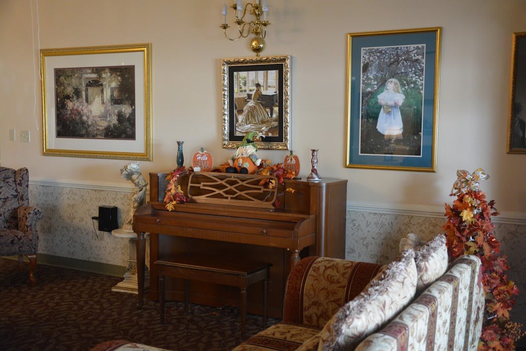 A cozy living room featuring a classic piano, adorned with decorative items and surrounded by artwork.