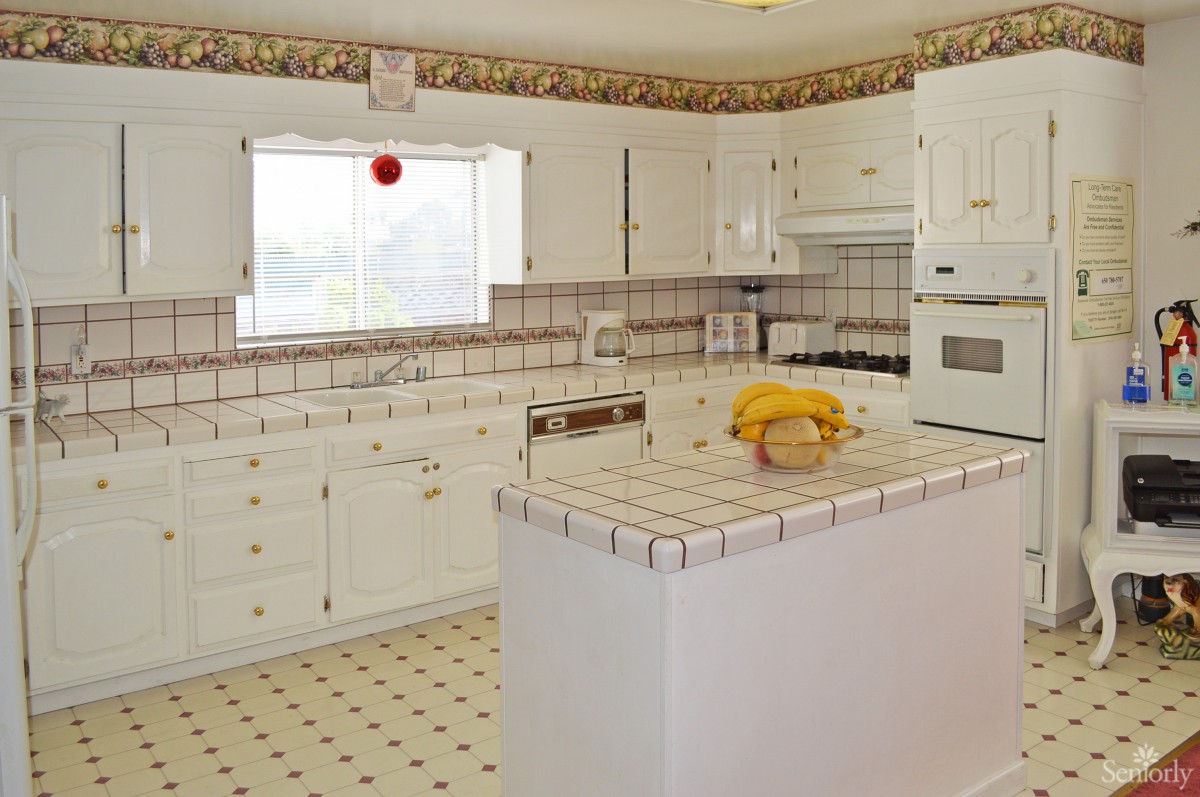 A spacious kitchen featuring white cabinets, tile countertops, and a central island with fruit on display.