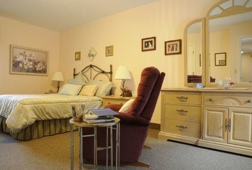 A cozy bedroom with a bed, recliner chair, and dresser featuring classic decor.