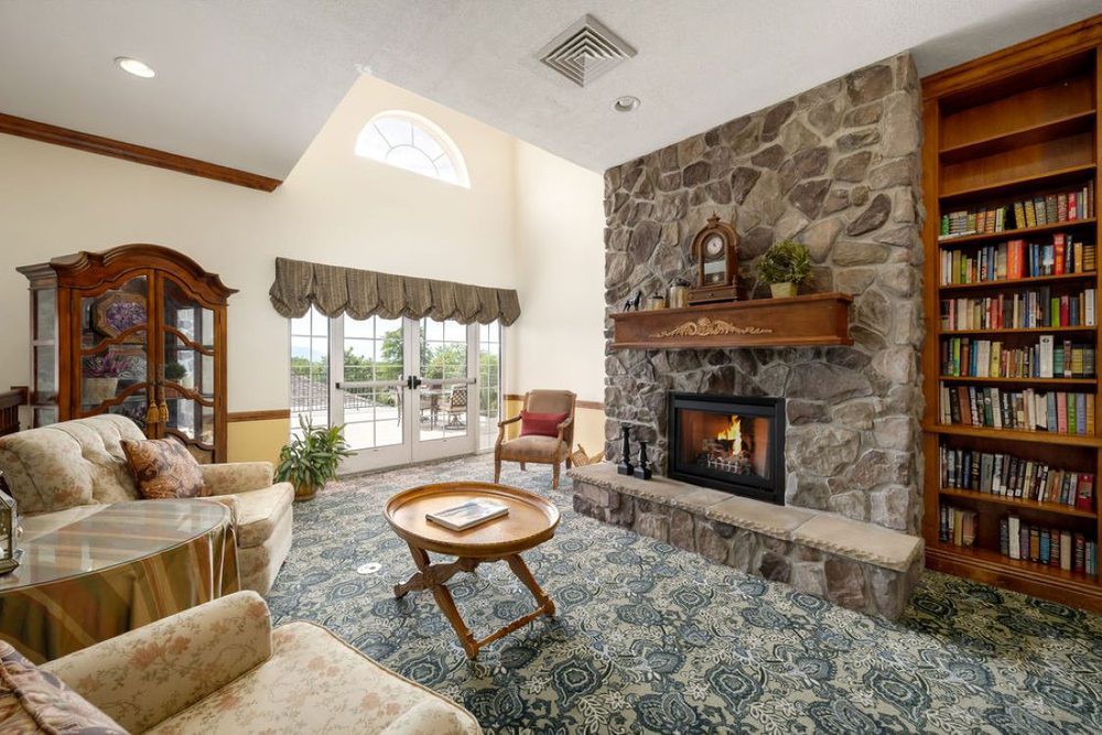 A cozy living room with a stone fireplace, comfortable seating, and large windows letting in natural light.