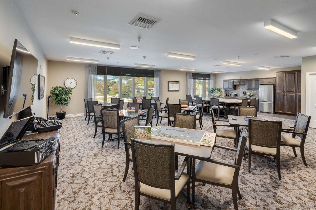 A spacious and well-lit dining area with multiple tables and chairs, surrounded by large windows and decorative plants.