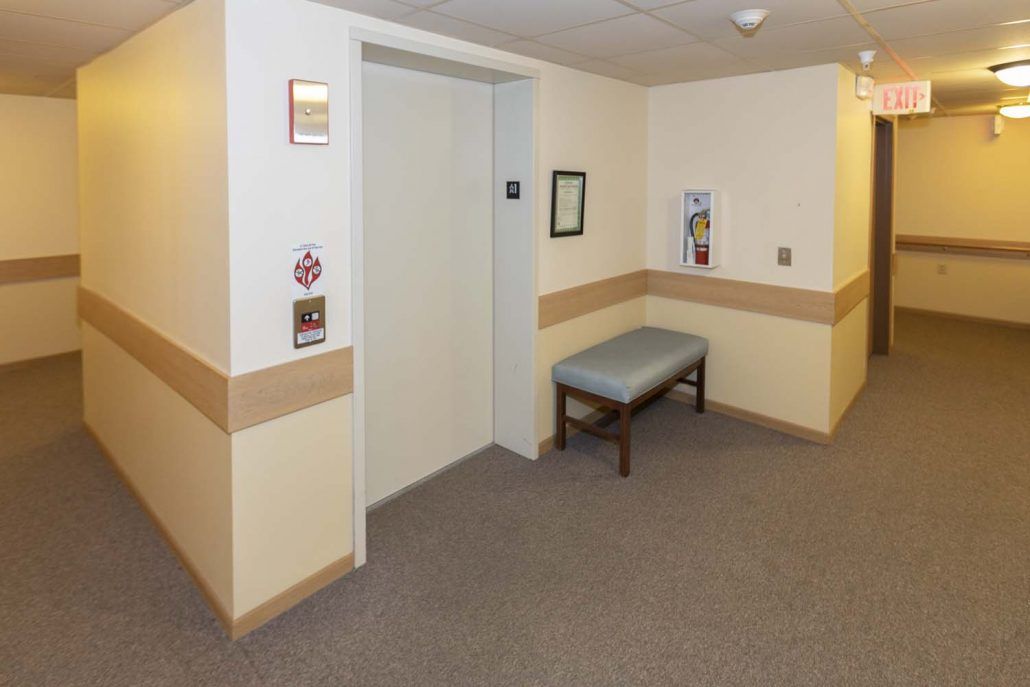 A hallway with an elevator and a bench on the side.