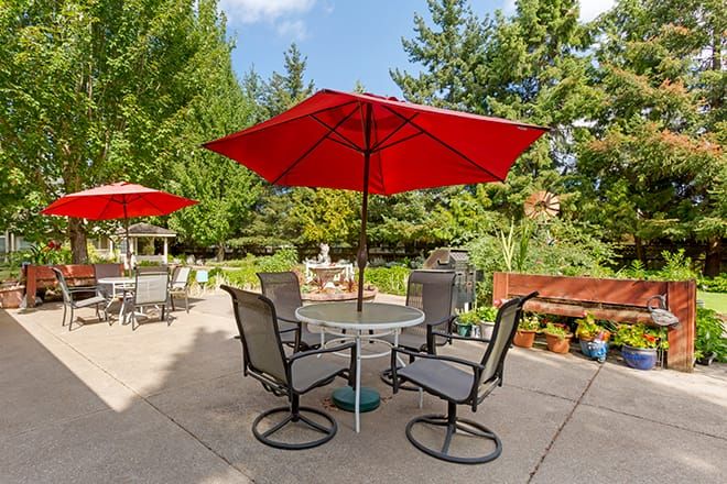 A peaceful outdoor patio area with a table, chairs, and a red umbrella, set in a lush garden setting.