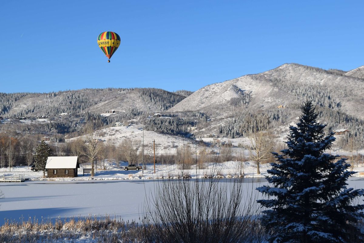 A hot air balloon floating over a snowy landscape with mountains in the background.