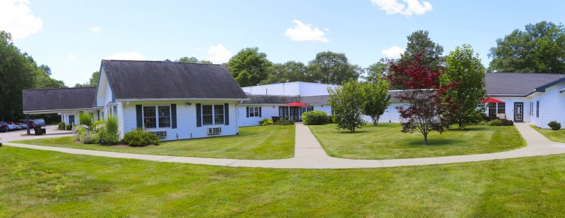 A building with a well-maintained lawn and pathway, surrounded by trees under a partly cloudy sky.