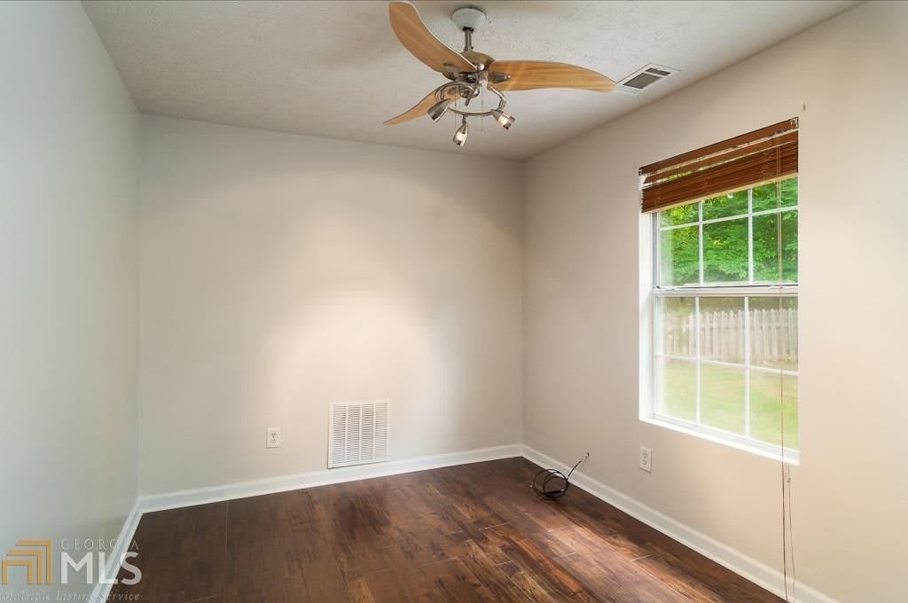 An empty room with a wooden floor and ceiling fan, featuring a window with blinds allowing natural light in.
