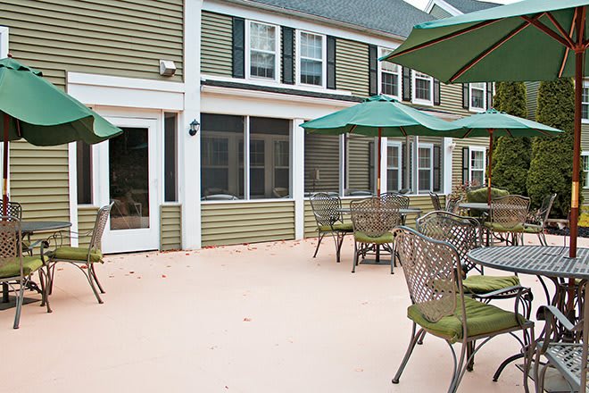 An outdoor patio area with tables, chairs, and green umbrellas in front of a building.