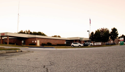 A view of a school building with parked vehicles and an American flag flying at sunset.