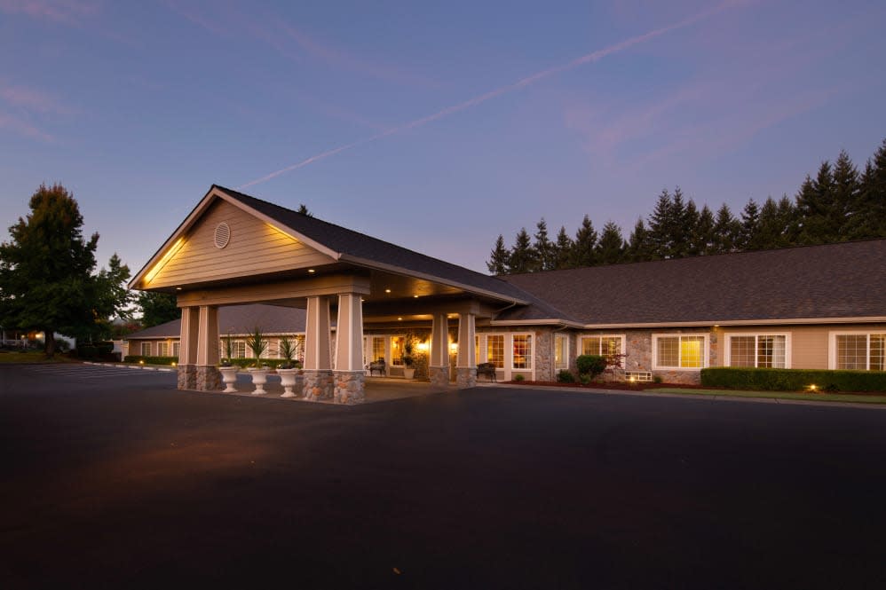 A well-lit building exterior during the evening with a parking lot in front and trees in the background.