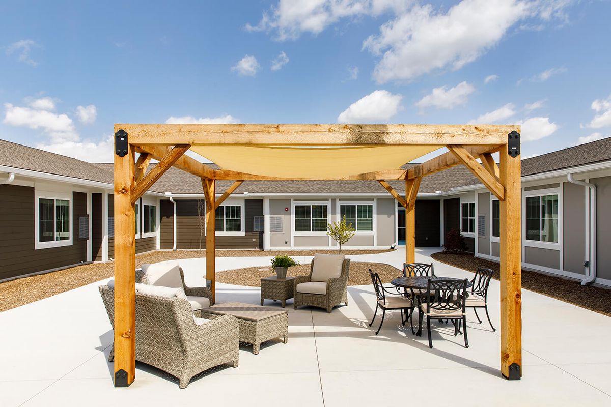 A sunny patio featuring a wooden pergola with outdoor seating and a table.