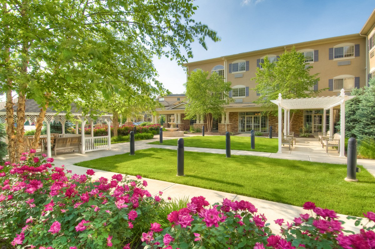 A beautifully landscaped outdoor area with vibrant flowers, lush green grass, and a modern building in the background.