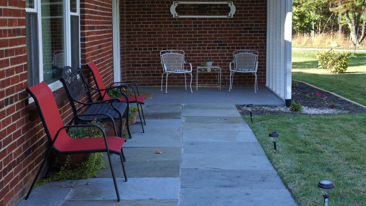 A porch with multiple chairs and a small table set against a brick wall.
