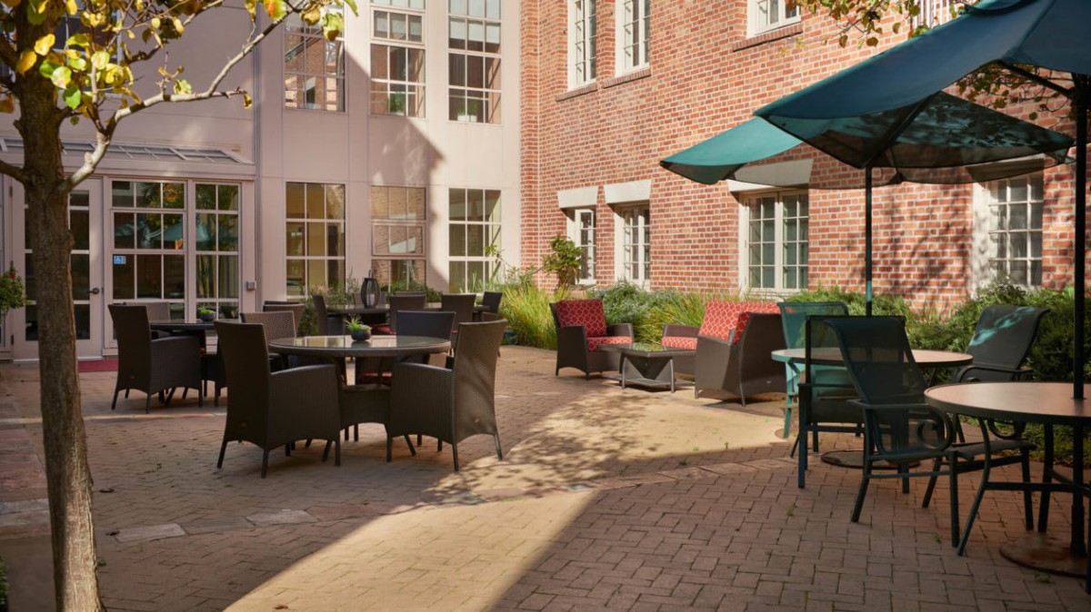 A sunlit courtyard with comfortable outdoor seating and tables, set against a brick building facade.