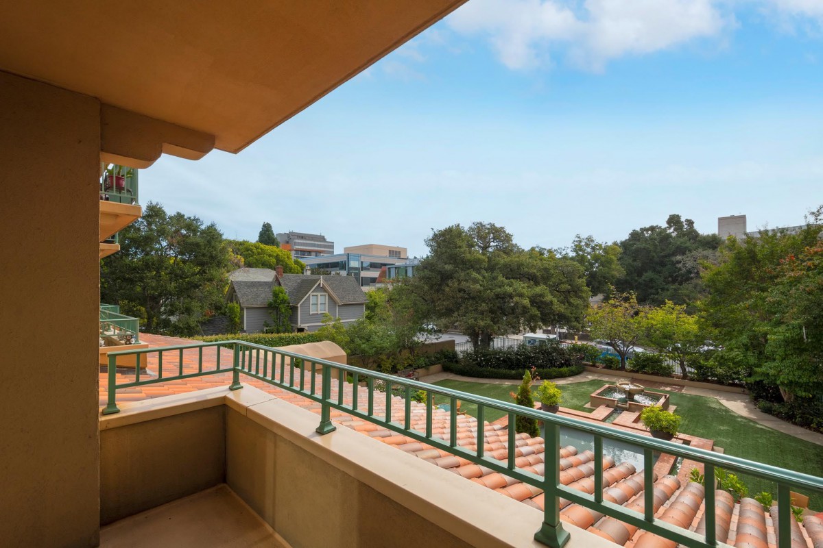 A scenic view from a balcony overlooking a neighborhood with lush trees and houses under a clear blue sky.
