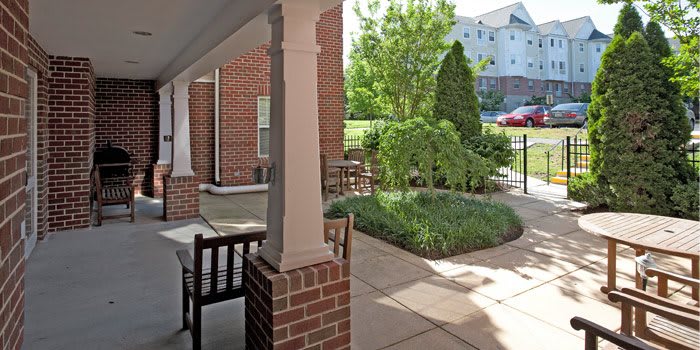 A sunny outdoor patio with garden furniture and lush greenery beside a brick building.
