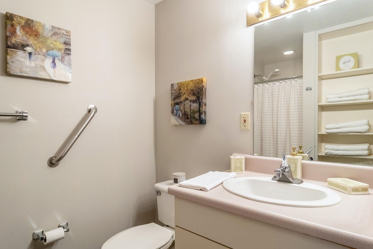 A small bathroom with a sink, toilet, mirror, and wall art.
