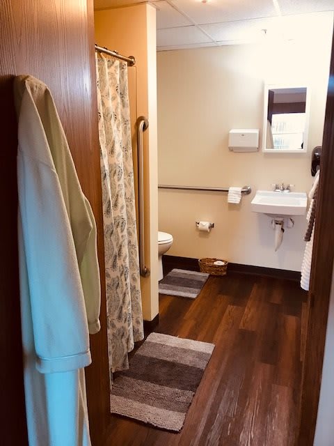 A cozy bathroom with wooden flooring, featuring a sink, mirror, and shower.