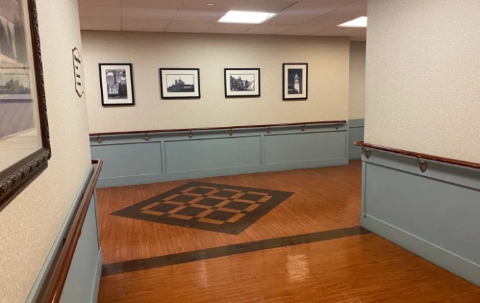 A hallway with wooden flooring, featuring framed photographs on the wall and subtle overhead lighting.