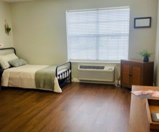 A simple and tidy bedroom with a single bed, window, and wooden furniture.