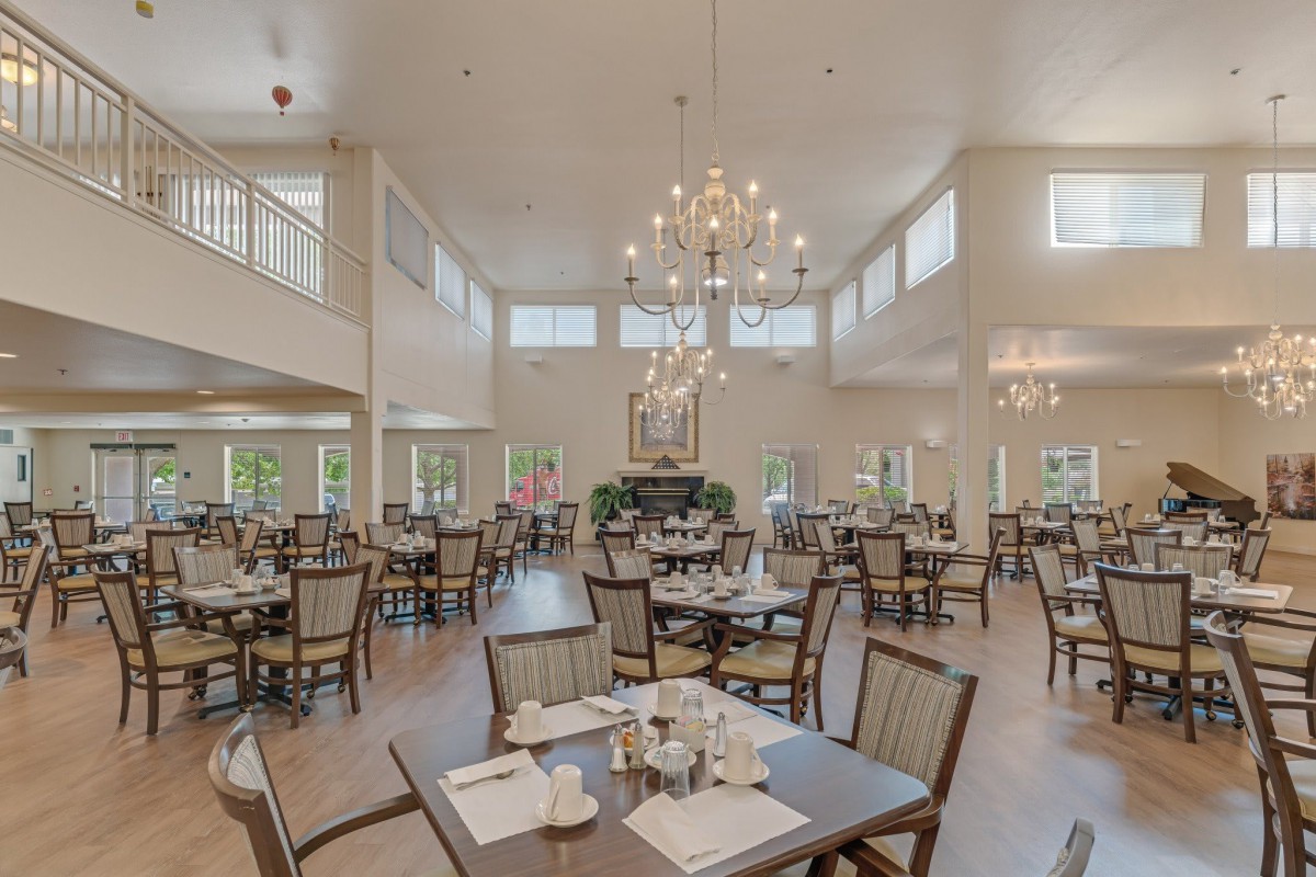 A spacious and elegantly designed dining room with multiple tables, chairs, large chandeliers, and abundant natural light.