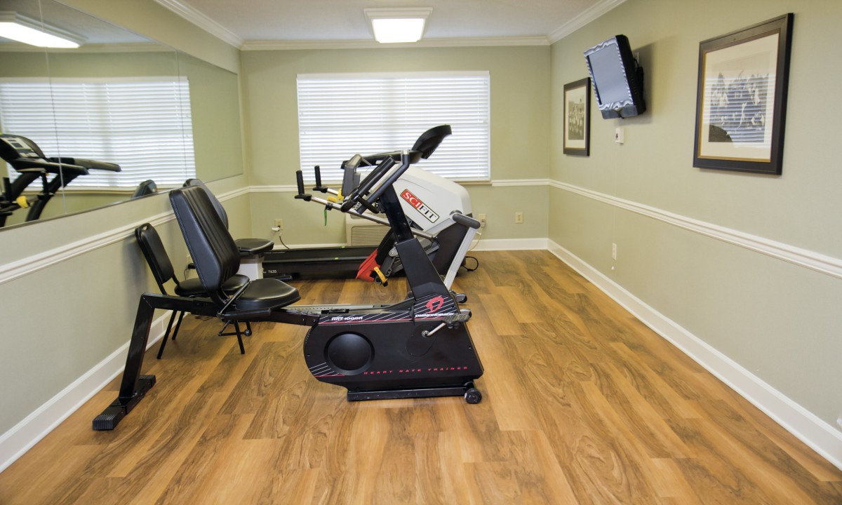 A small exercise room with a stationary bike, treadmill, and a wall-mounted television.