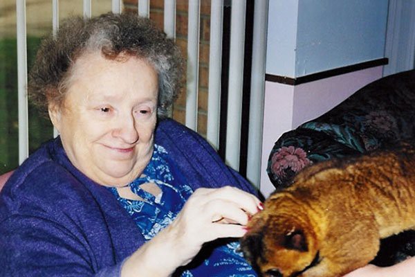 An elderly woman is smiling while petting a cat indoors.