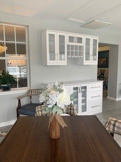 A cozy dining area with a wooden table, plaid chairs, and white cabinets adorned with flowers.