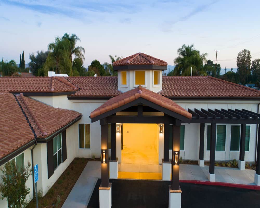 A beautiful house with a warm entrance and tiled roof, surrounded by palm trees in the evening.