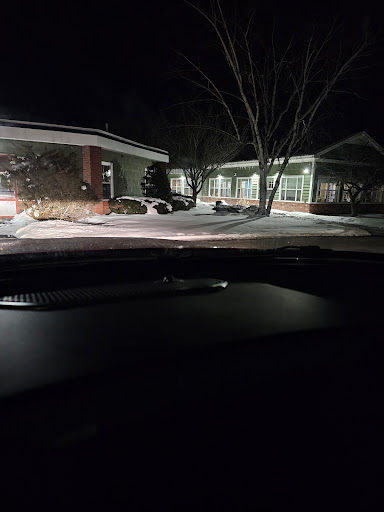 A nighttime view of a snow-covered area with buildings, seen from inside a car.