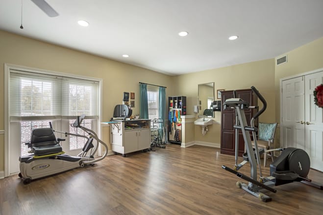 A well-lit home gym with various exercise equipment and a wooden floor.