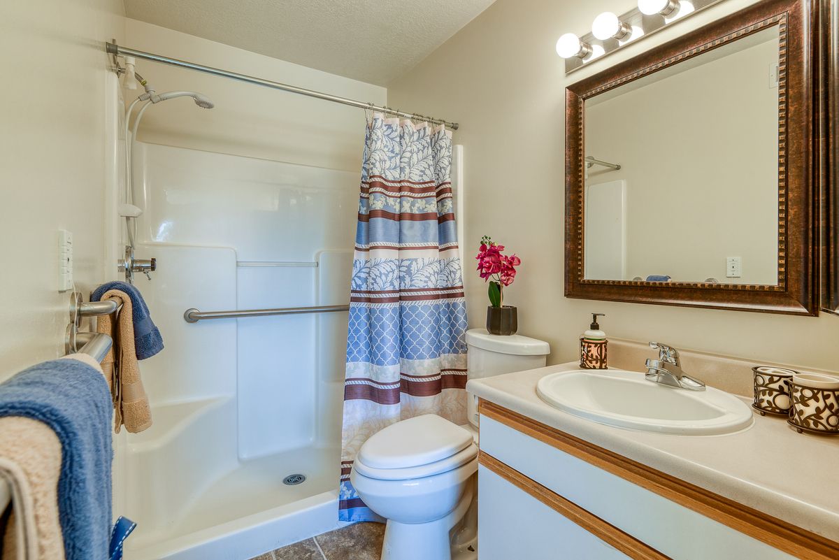 A clean and well-lit bathroom featuring a shower with a patterned curtain, a toilet, and a sink with a mirror above it.