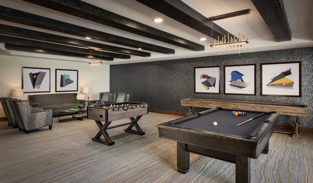 A modern game room featuring a pool table and foosball table, with sleek interior design and contemporary artwork on the walls.