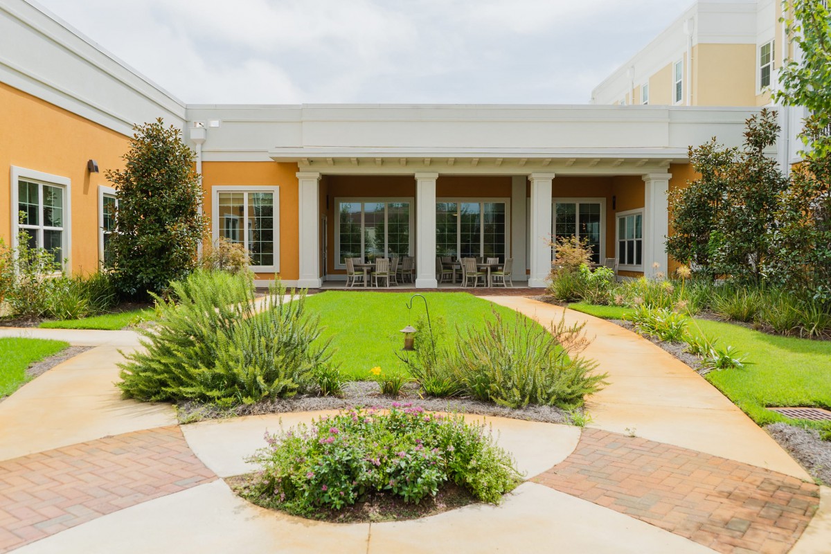 A beautifully landscaped garden with a patio and lush green lawn in front of a building.