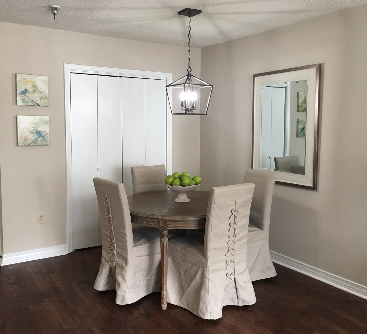 A cozy dining room with a round table, covered chairs, and a modern chandelier.