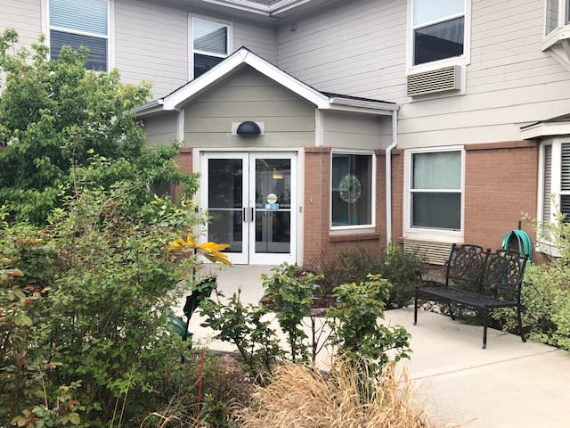 The image shows the exterior entrance of a building with surrounding landscaping and shrubs.