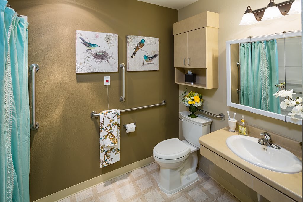 A well-decorated bathroom featuring a toilet, sink, and mirror, complemented by artwork and fresh flowers.