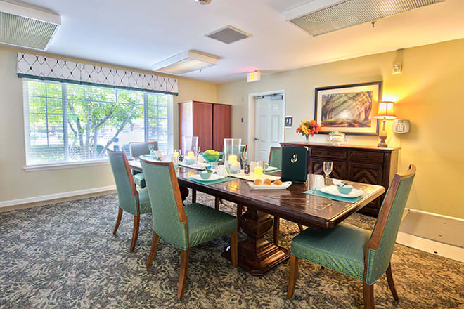 A well-decorated dining room with a large table and chairs, featuring natural light from a broad window.