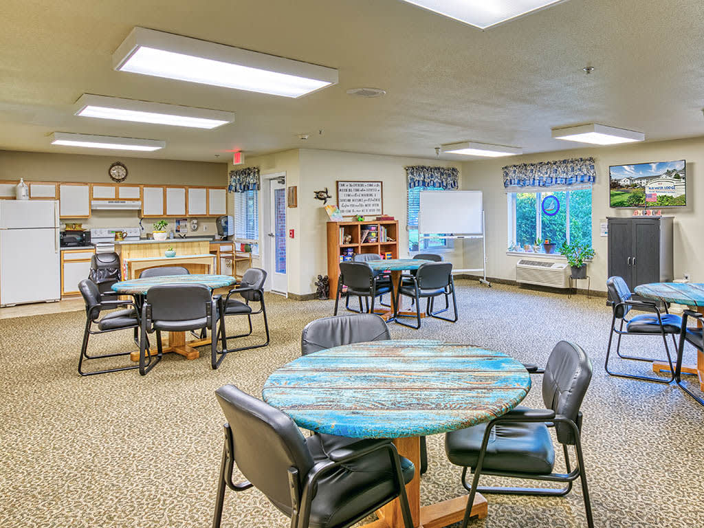 A brightly lit community center meeting room with tables and chairs arranged for group activities.