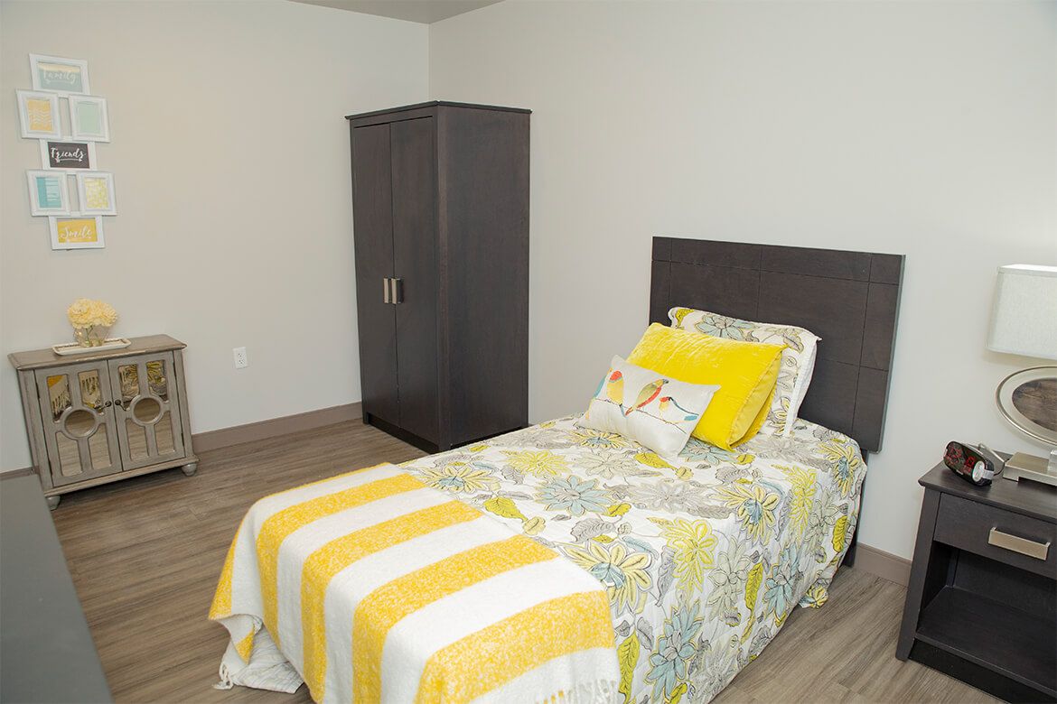 A minimalist bedroom with a single bed featuring yellow bedding and a dark wardrobe.